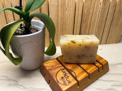 Bar of soap on a wooden soap dish with a plant in the background